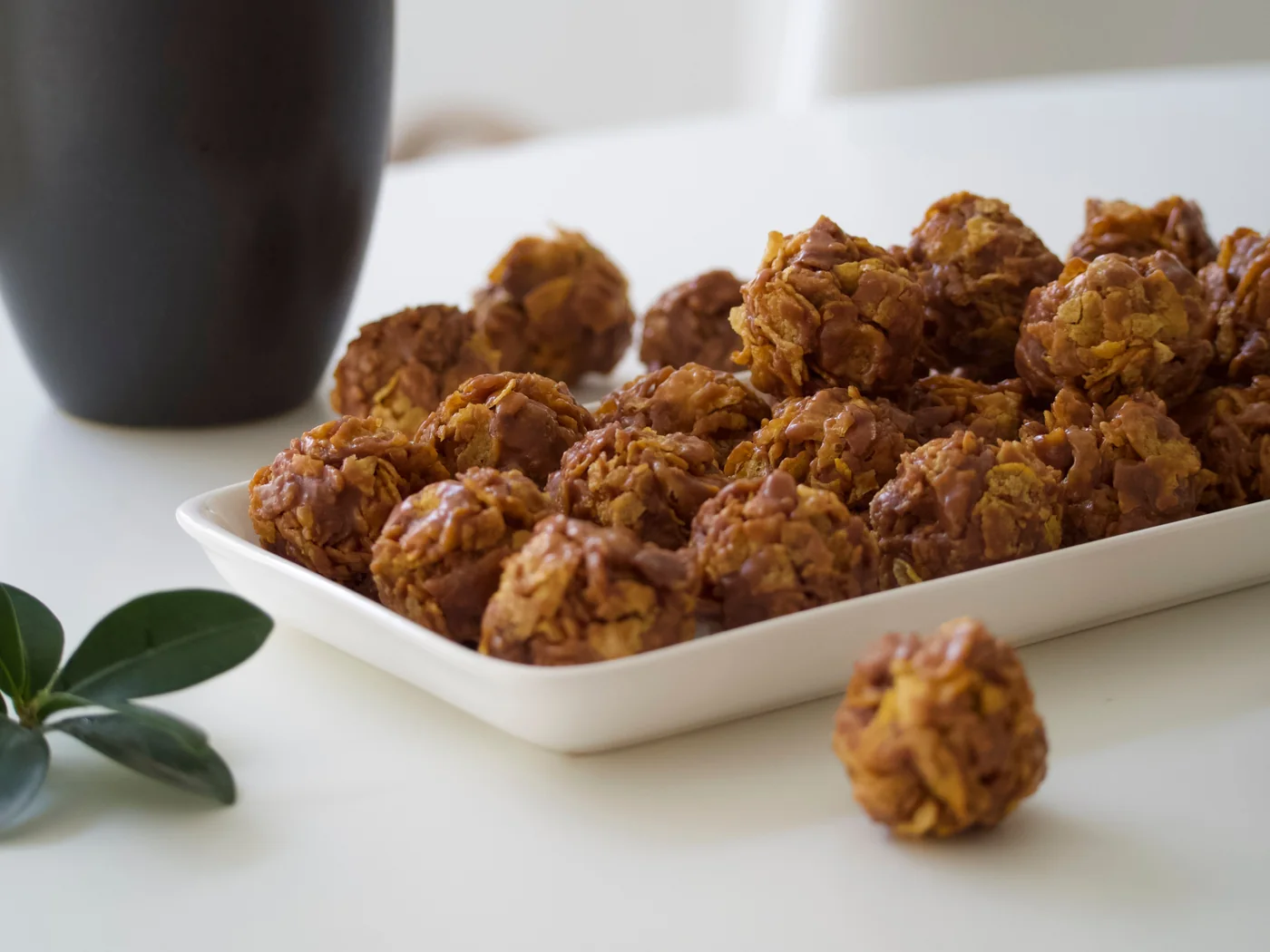 Chocolate cornflake cakes piled on a white plate beside a mug of tea