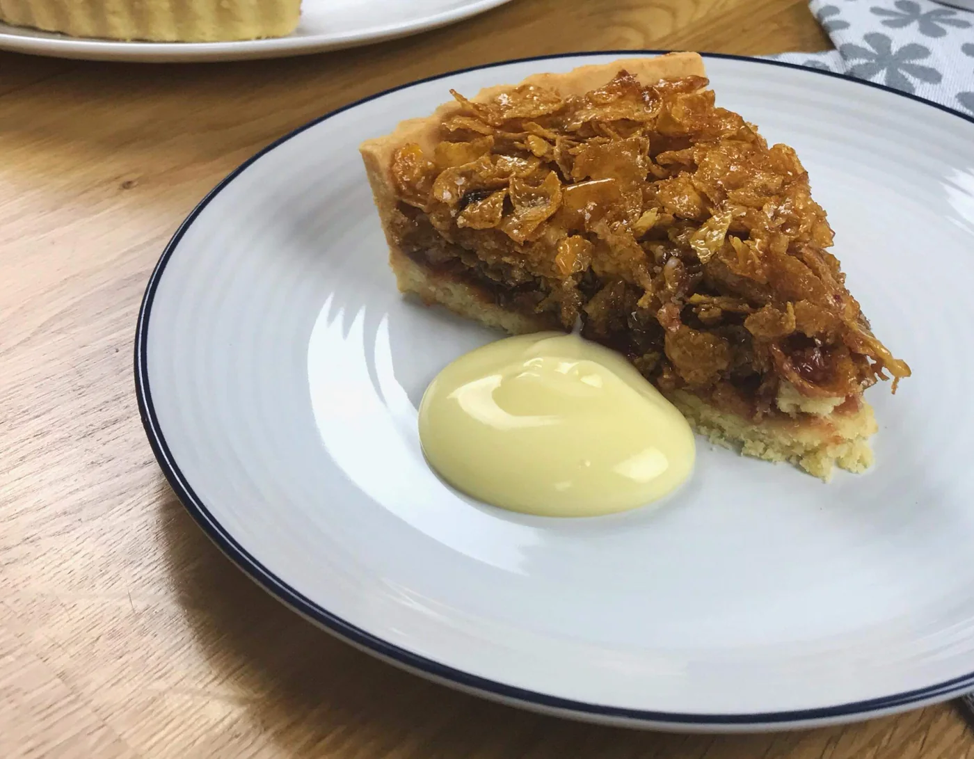 Slice of cornflake tart with custard, showing the jam layer and golden cornflake topping