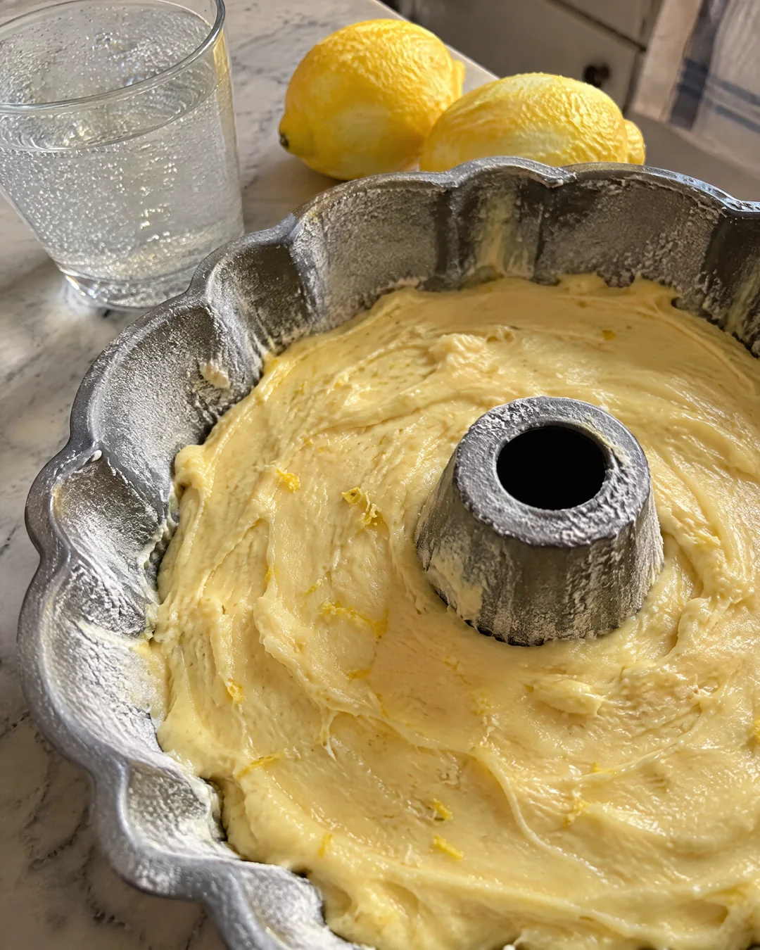 Pale pound cake batter in a fluted Bundt pan, flecked with lemon peel, ready for the oven