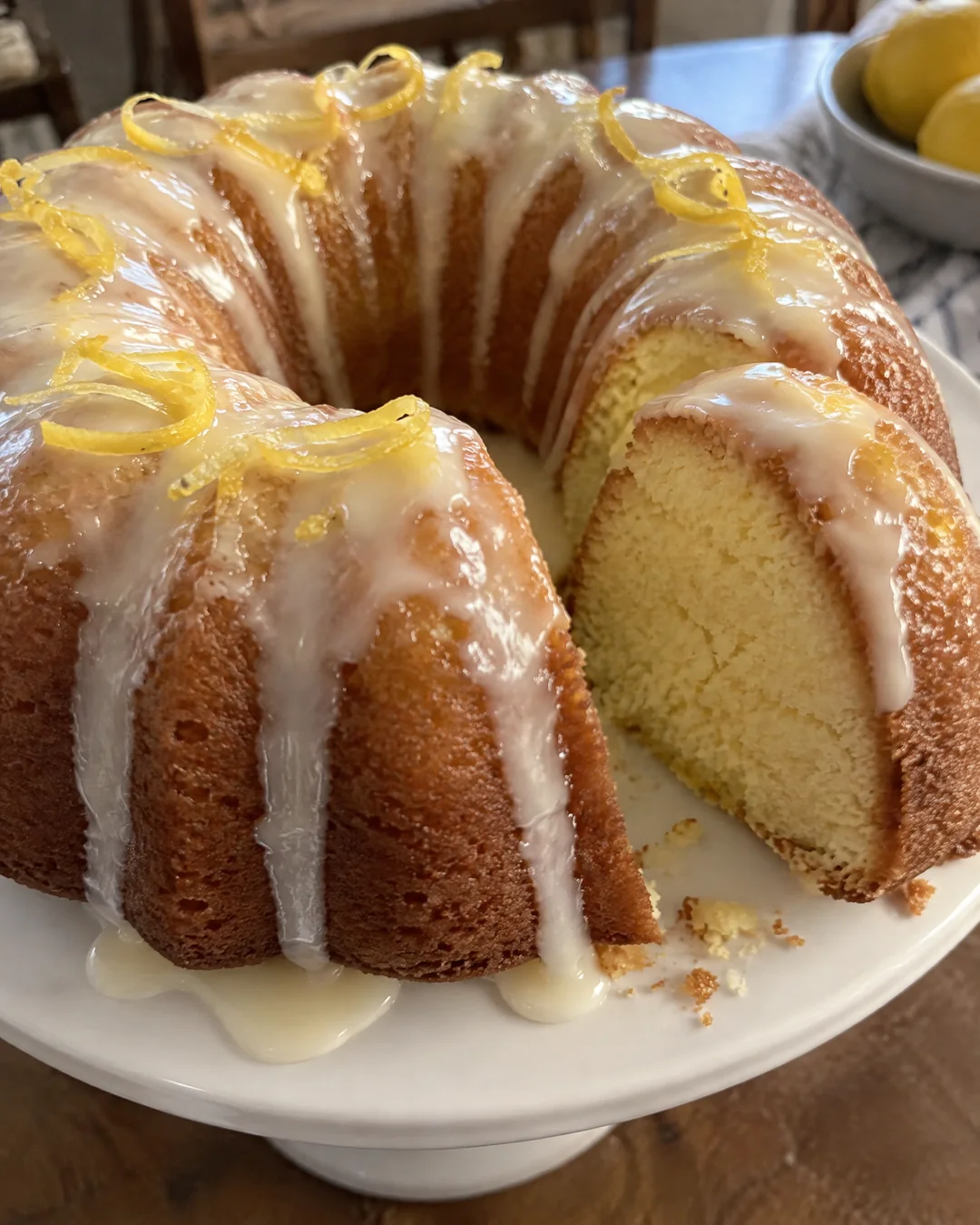 A whole glazed 7UP pound cake on a cake stand with a wedge cut out to show the fine crumb