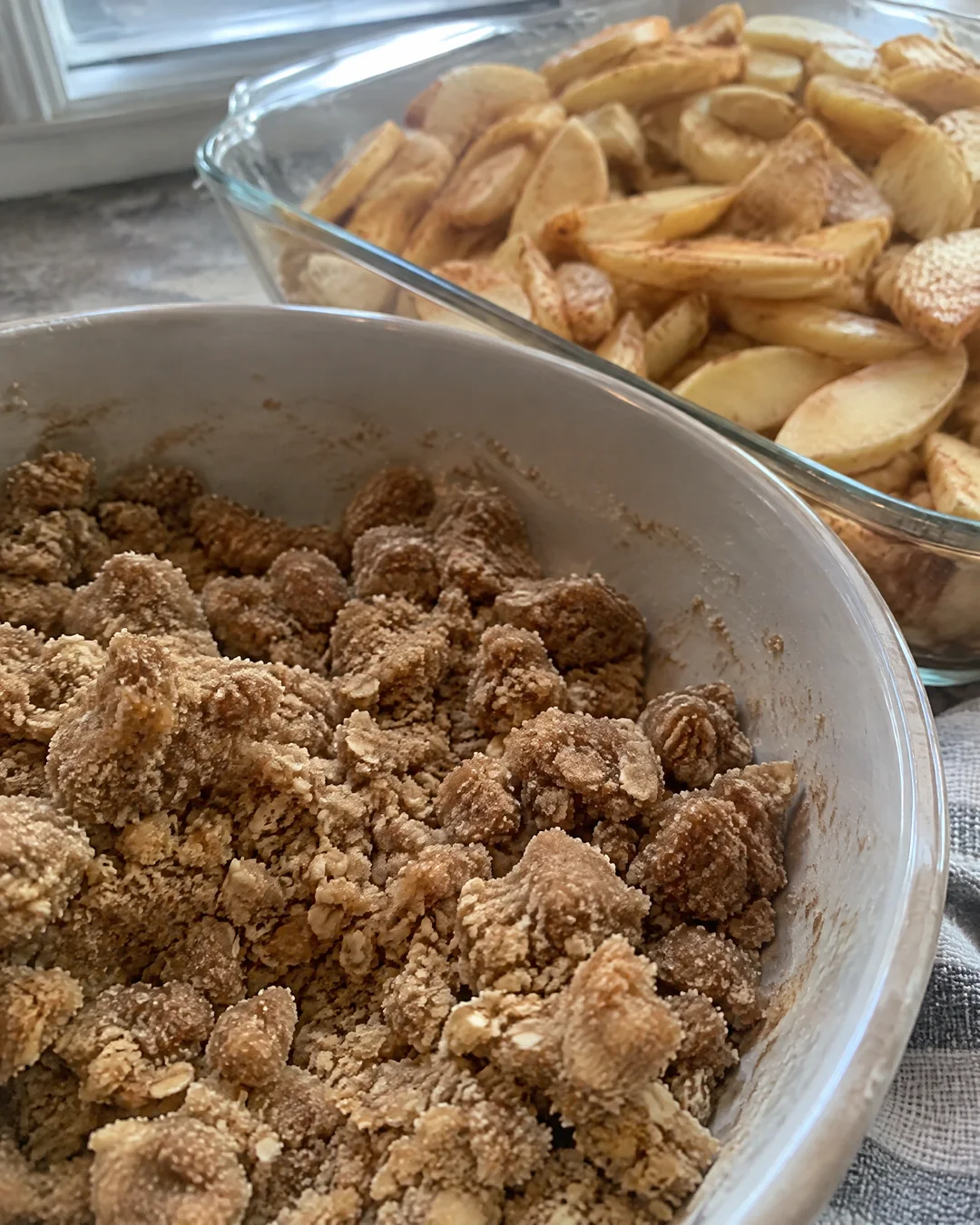 Big lumps of brown sugar crumb topping in a bowl beside a pan of apple slices