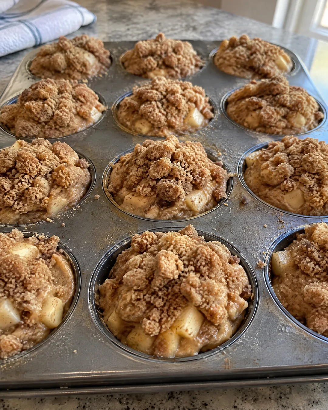 Muffin tin filled to the brim and covered with crumb topping before baking