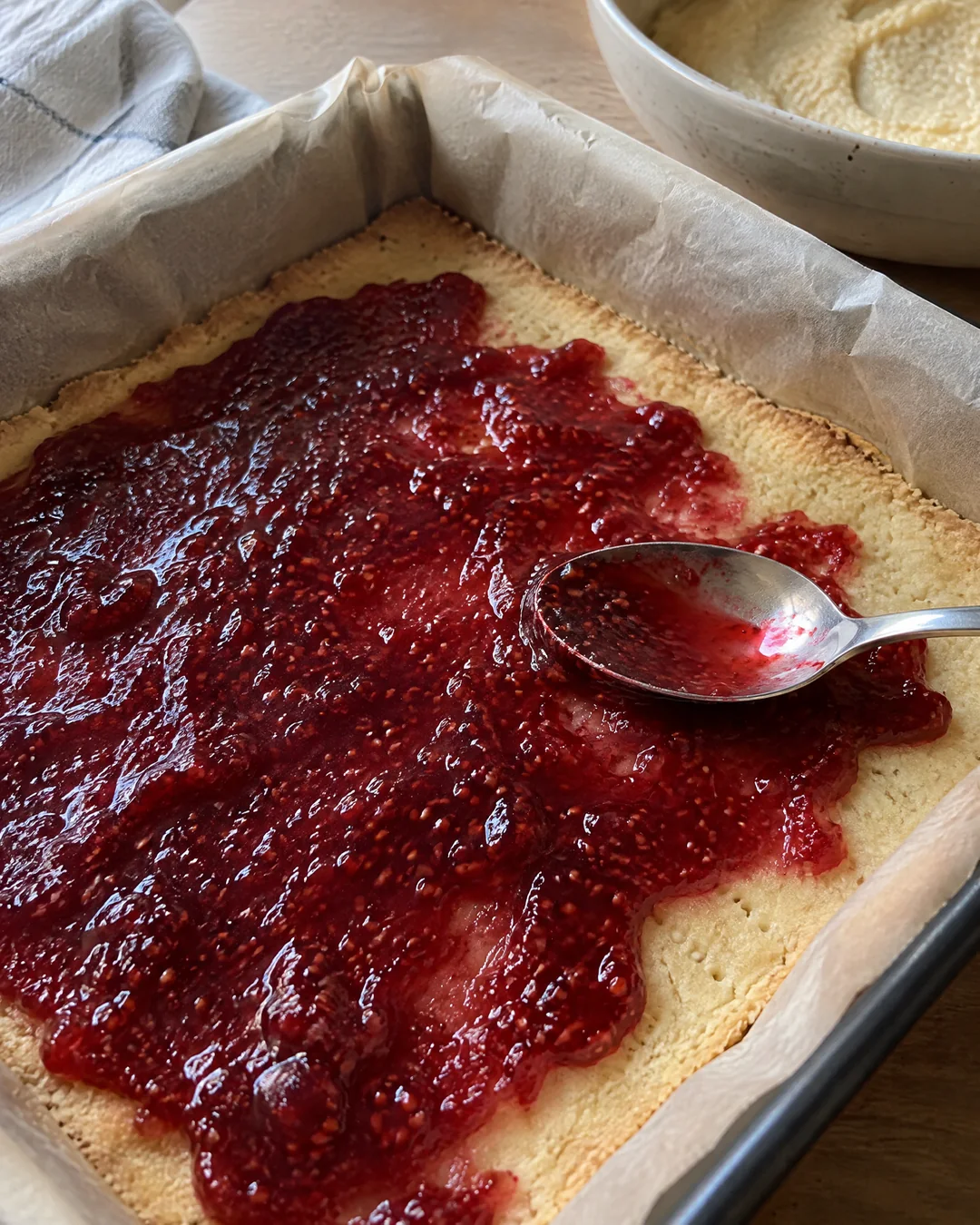 A blind-baked shortcrust base in a square pan spread with a thin layer of raspberry jam