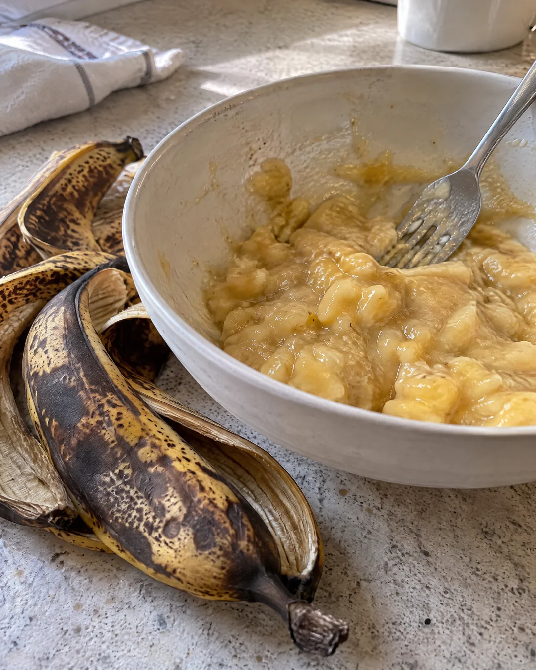 Black ripe bananas being mashed with a fork in a mixing bowl
