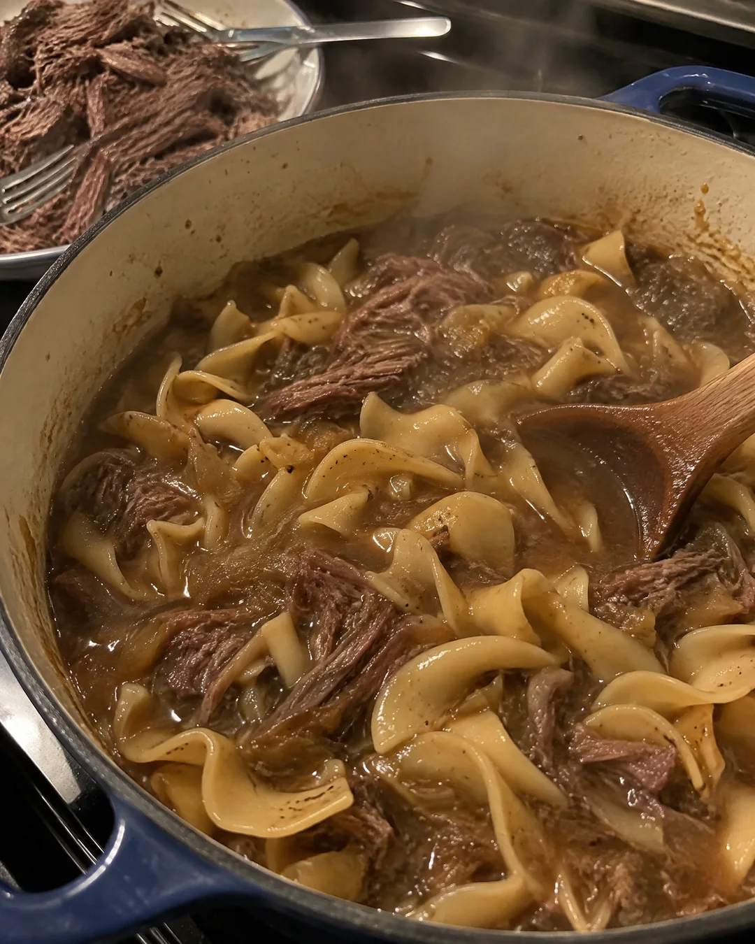 Thick egg noodles simmering in beef broth in a Dutch oven as the broth turns to gravy