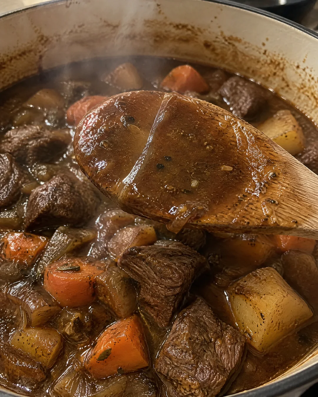 Thick beef stew gravy coating the back of a wooden spoon over a pot