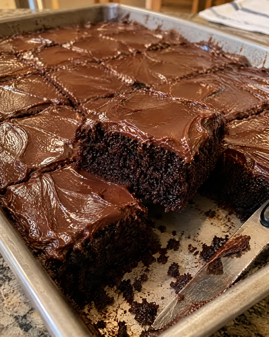A frosted black magic sheet cake cut into squares in its pan