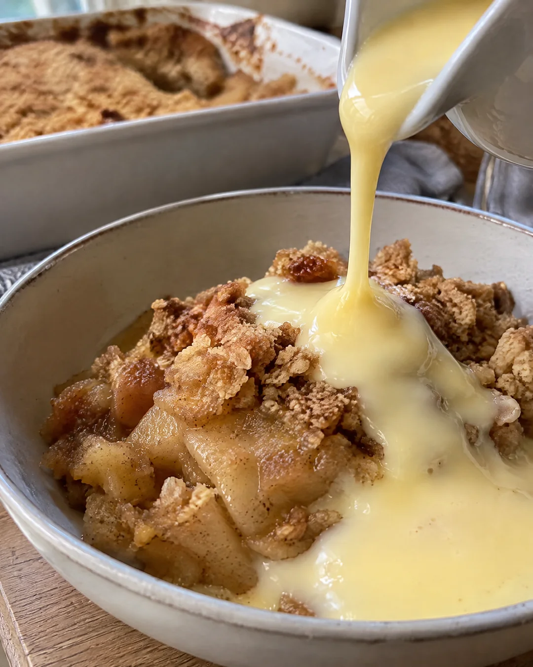 Pouring hot custard from a jug over a bowl of apple crumble