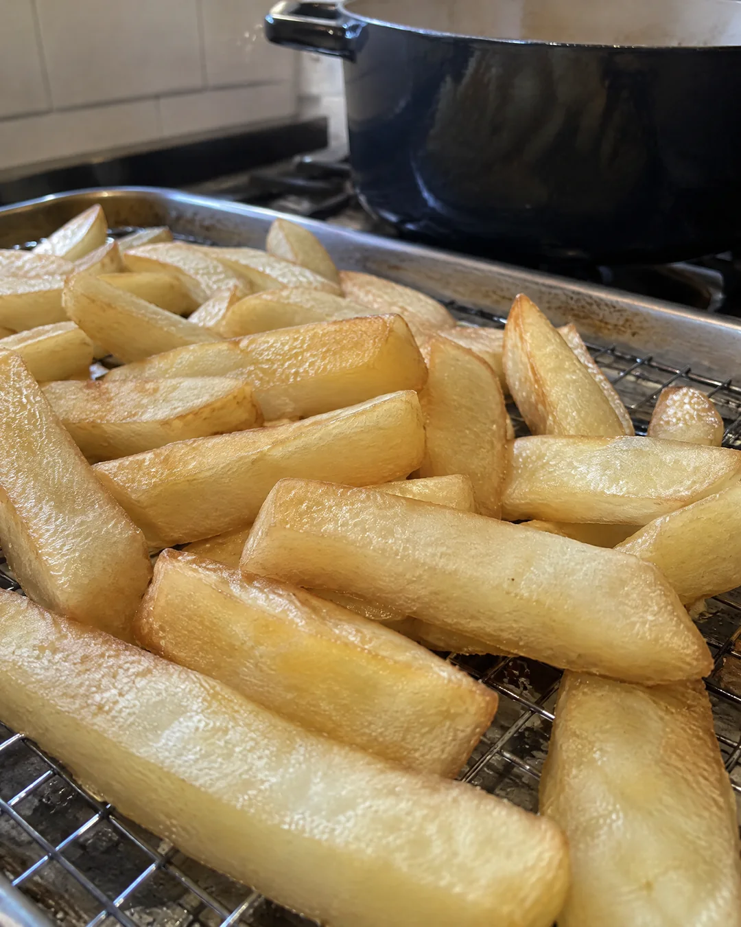 Thick-cut potato chips resting on a rack after their first fry