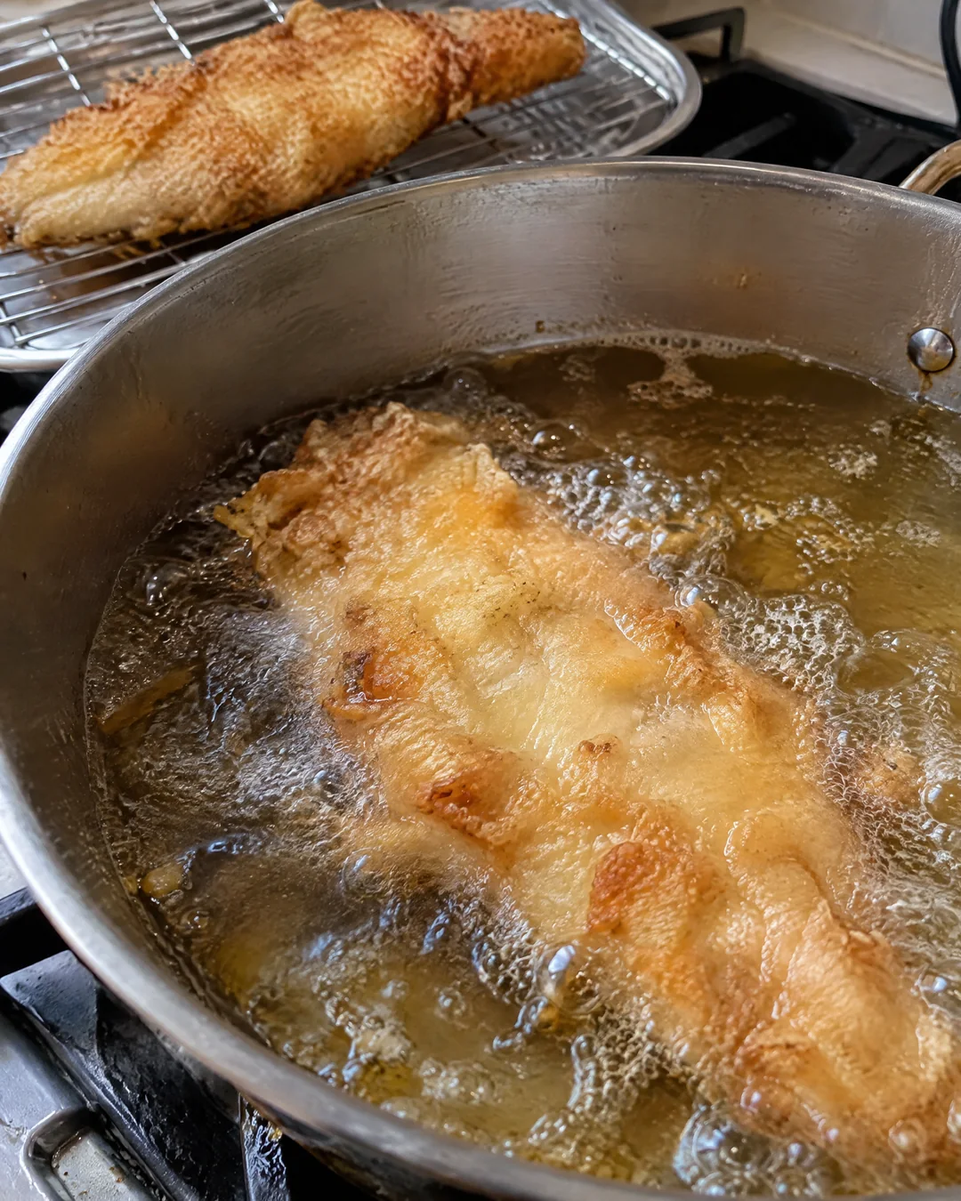 Battered fish frying golden in a pot of hot oil