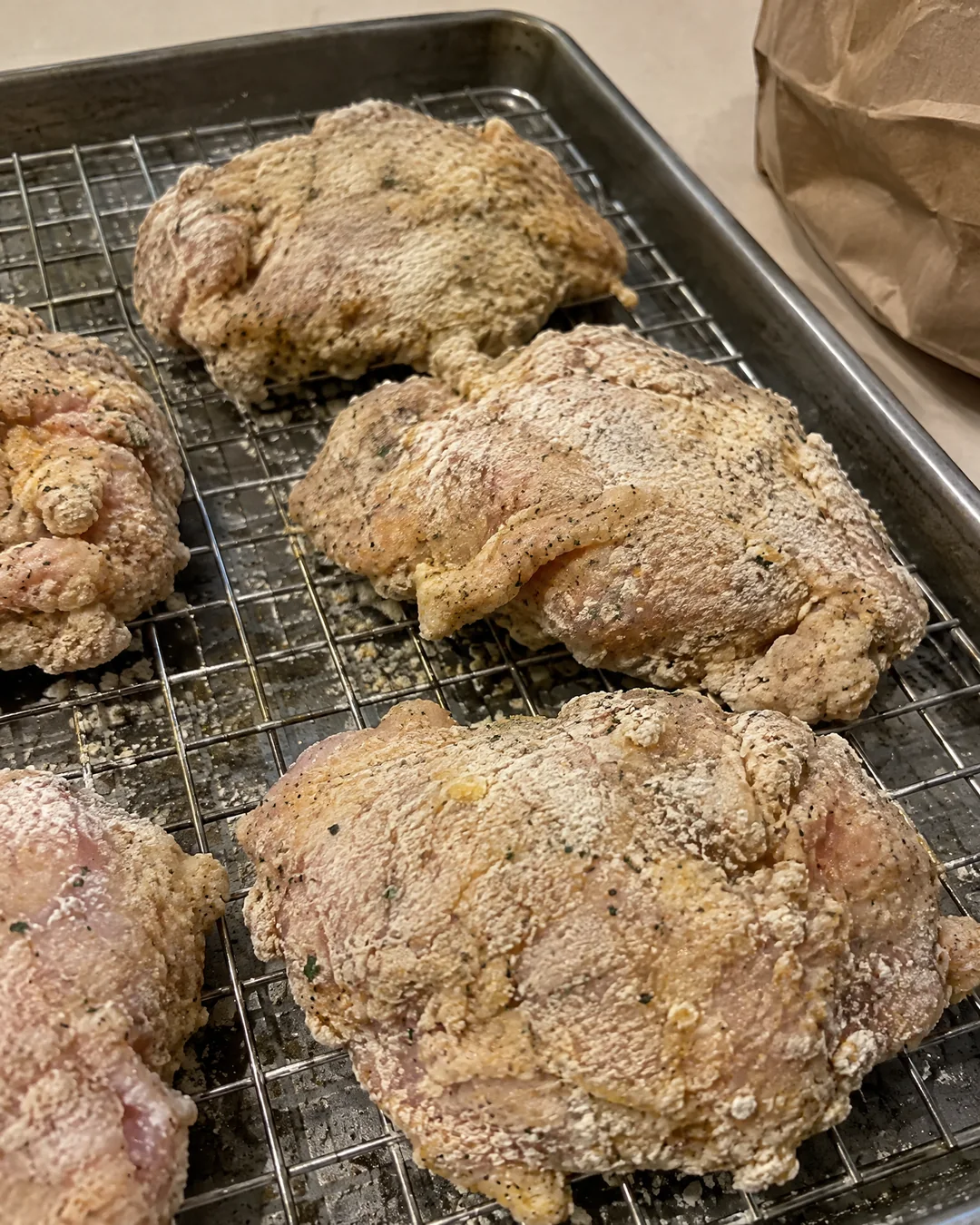 Floured chicken pieces resting on a wire rack so the coating sets before frying
