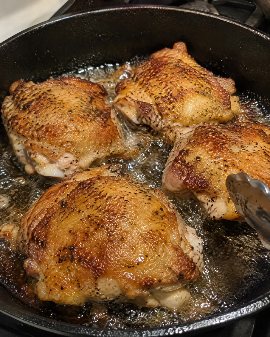Fried chicken frying in an inch of oil in a black cast iron skillet