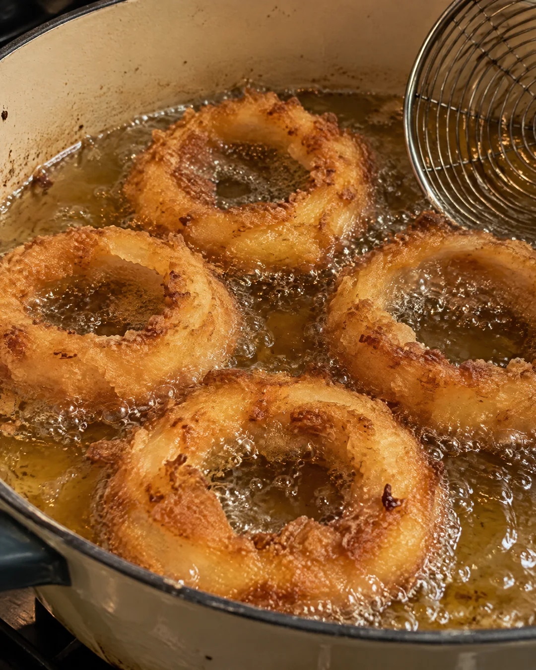 Golden crispy buttermilk onion rings frying in a pot of hot oil