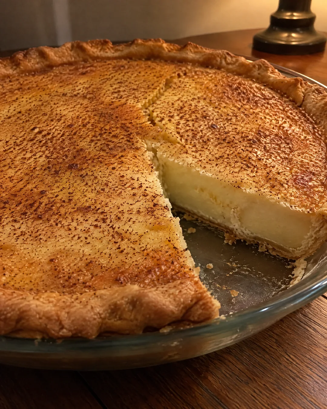 A baked buttermilk pie with a golden freckled top and a slice removed