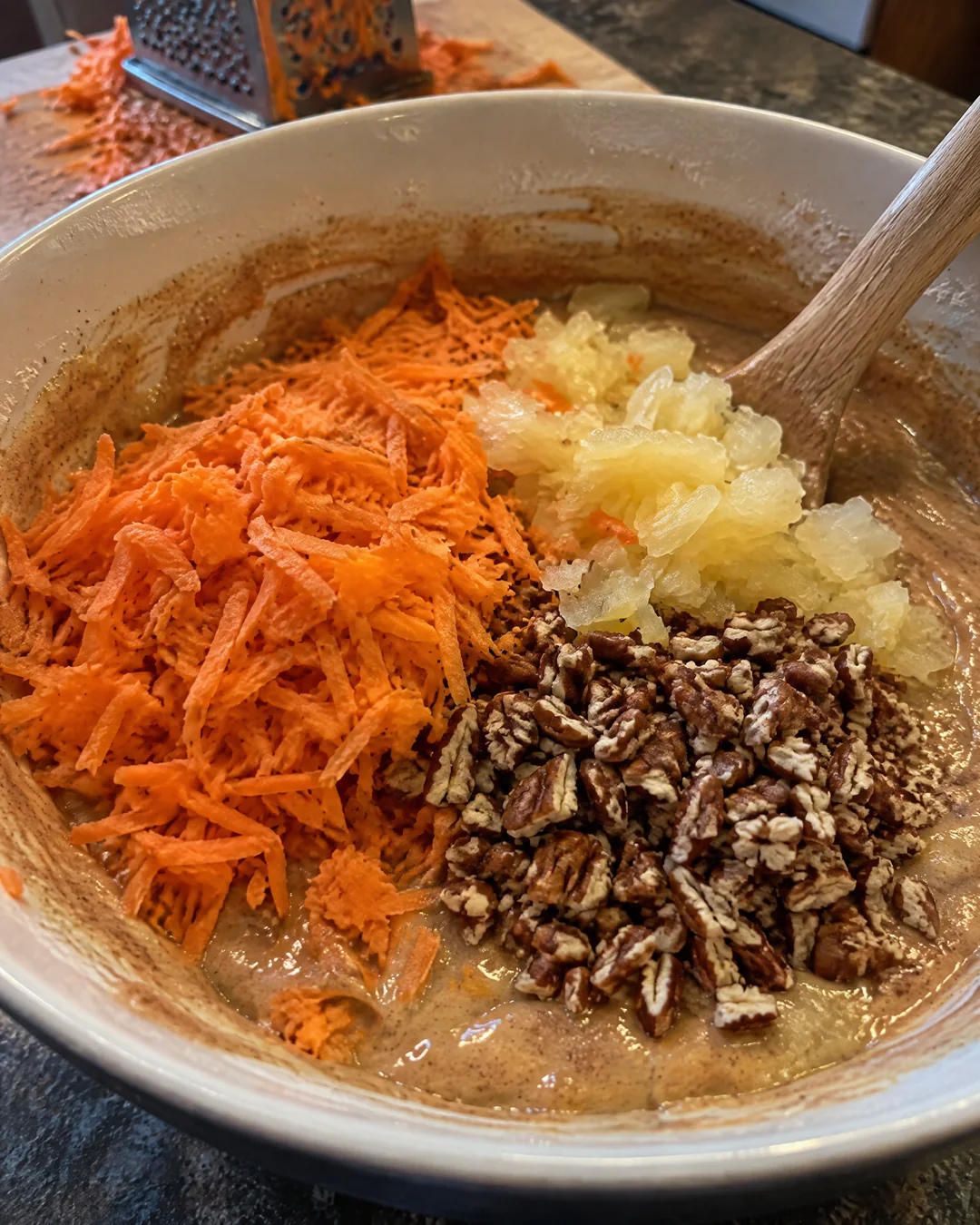 Finely grated carrots, drained crushed pineapple and chopped pecans being folded into carrot cake batter