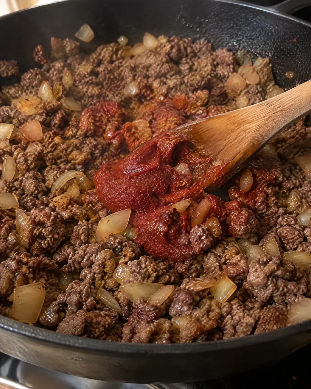Browned ground beef and onion with tomato paste in a skillet for cheeseburger macaroni