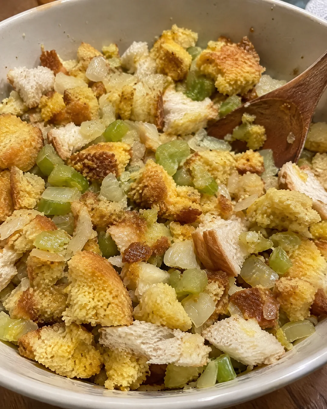 Crumbled day-old cornbread with cooked onion and celery in a large mixing bowl