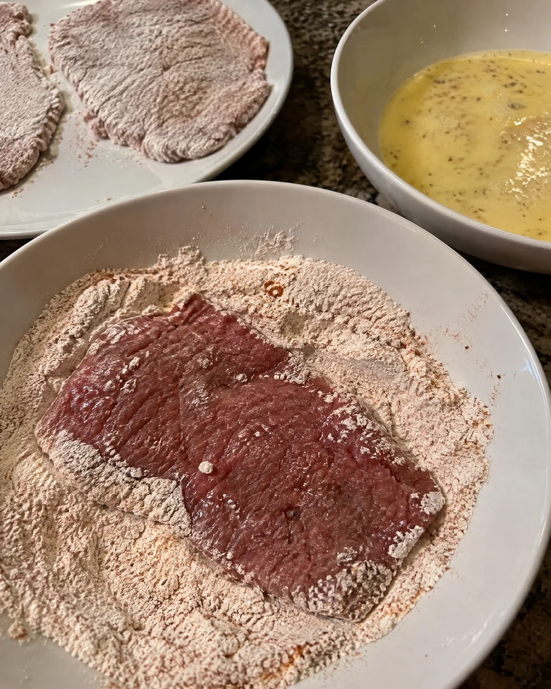 Cube steak pressed into seasoned flour for the second dredge, bowls of flour and buttermilk egg