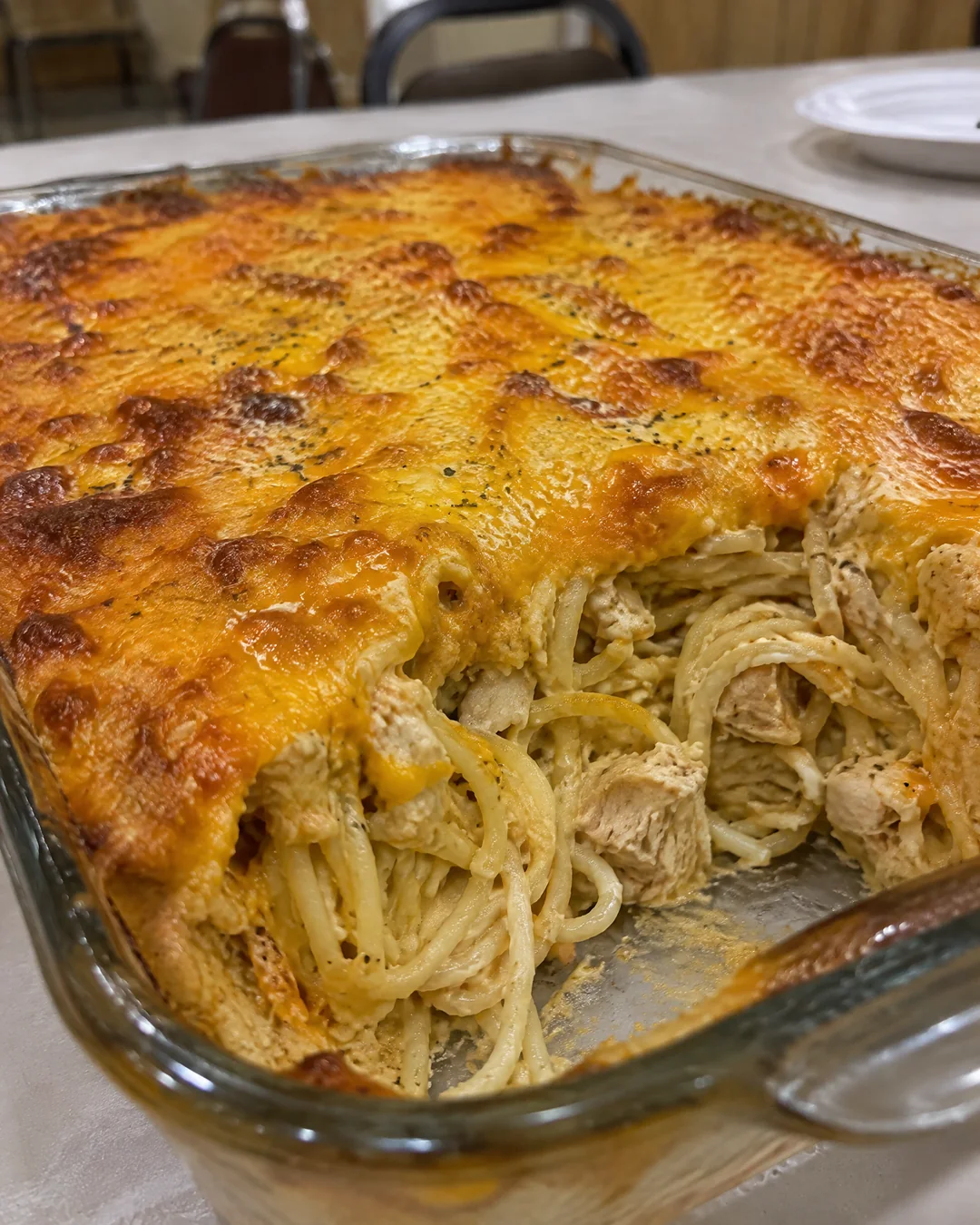 Baked chicken spaghetti casserole with a bubbling melted cheddar top in a glass dish