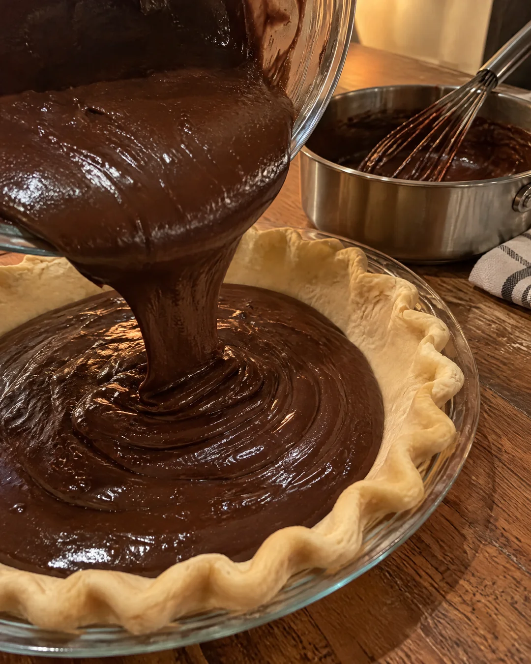 Glossy chocolate fudge pie filling being poured into a pie crust