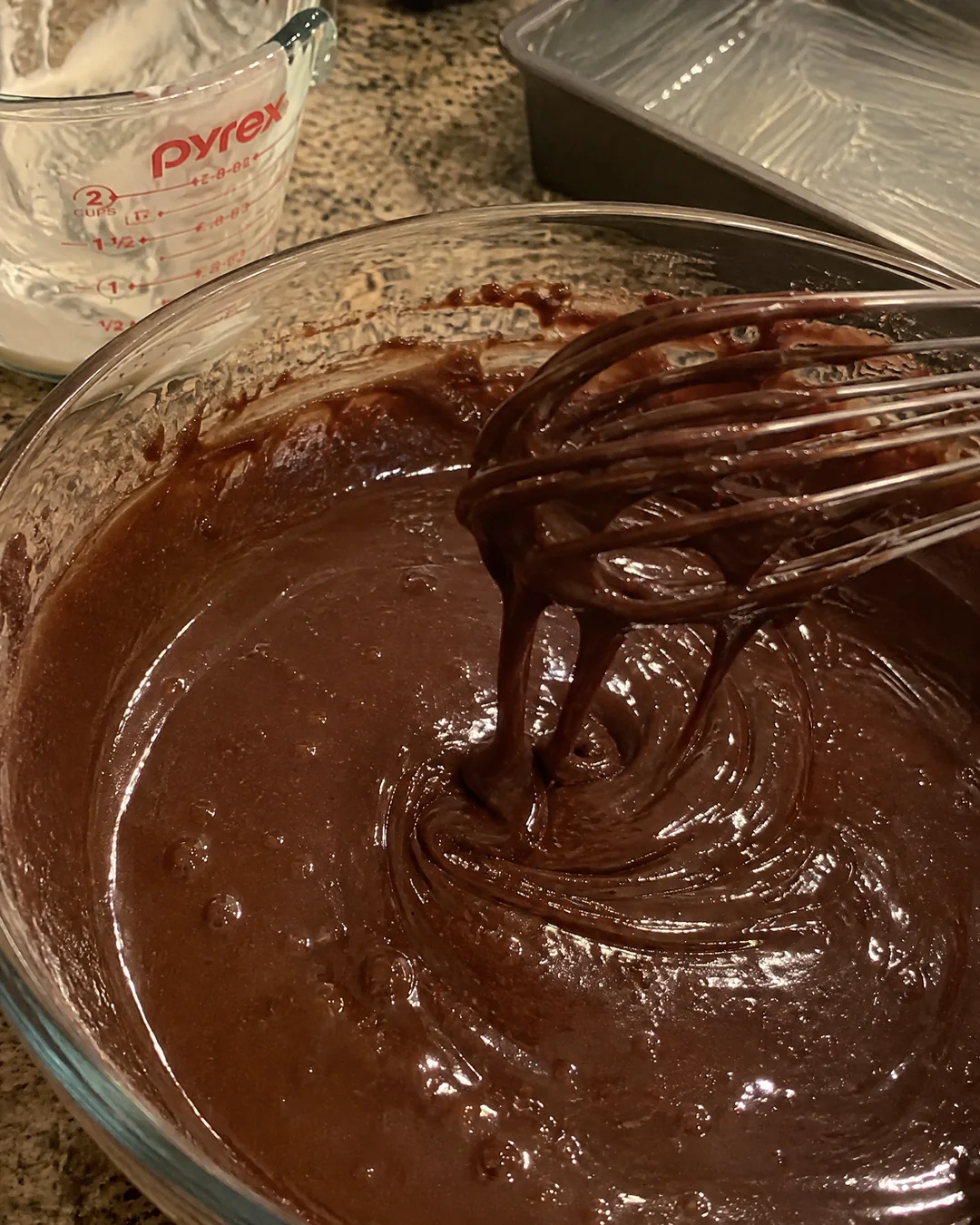 Glossy dark chocolate cake batter in a mixing bowl with a whisk, smooth and ready to pour