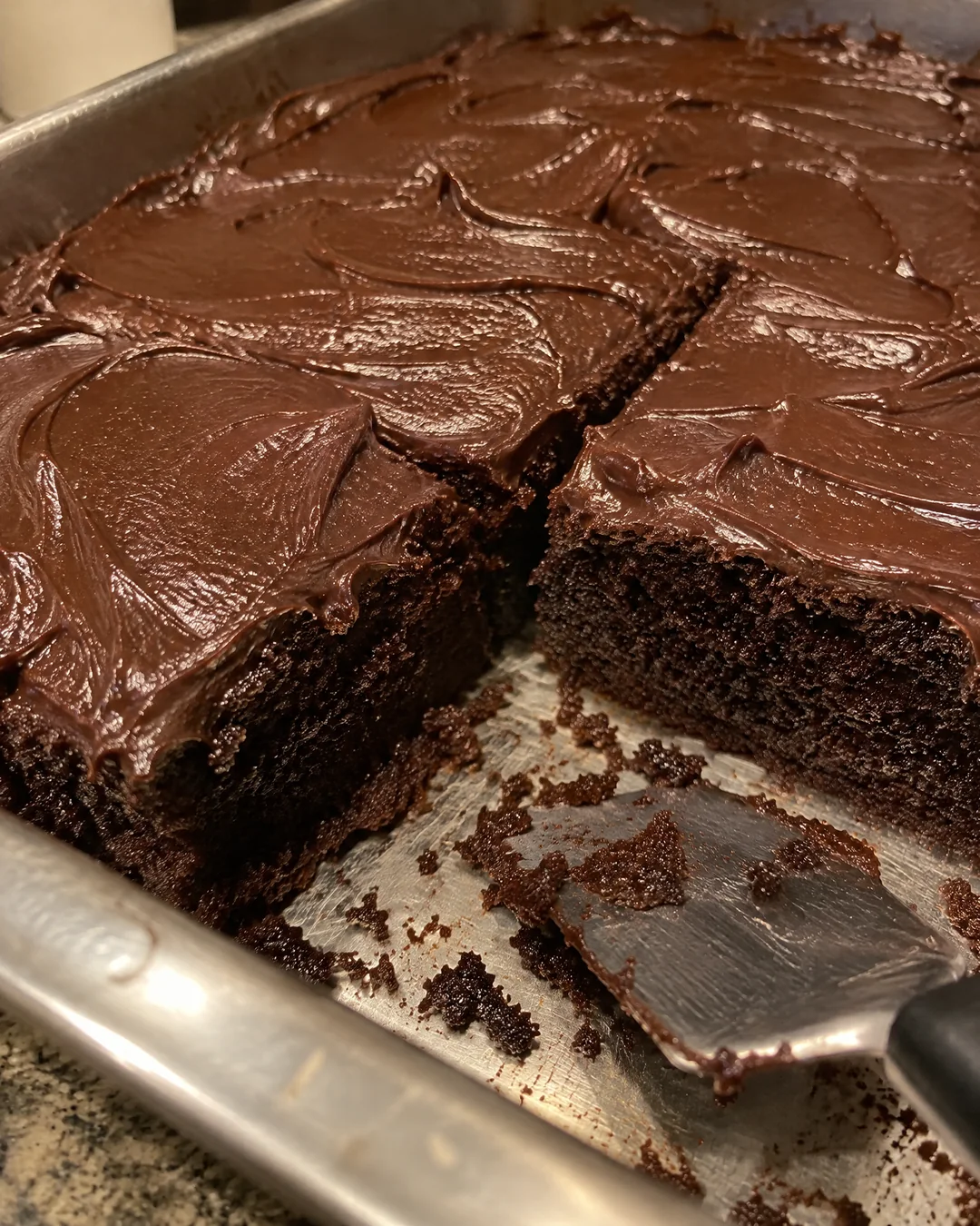 A frosted chocolate mayonnaise cake in its 9 by 13 pan with two squares cut out, showing the dark moist crumb