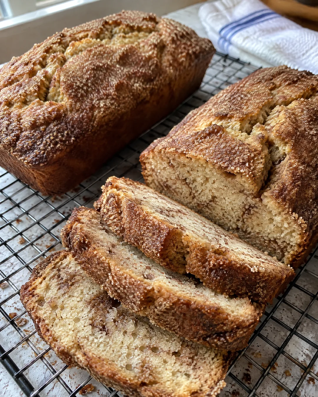 Two baked cinnamon sugar friendship bread loaves on a rack, one sliced to show the soft crumb