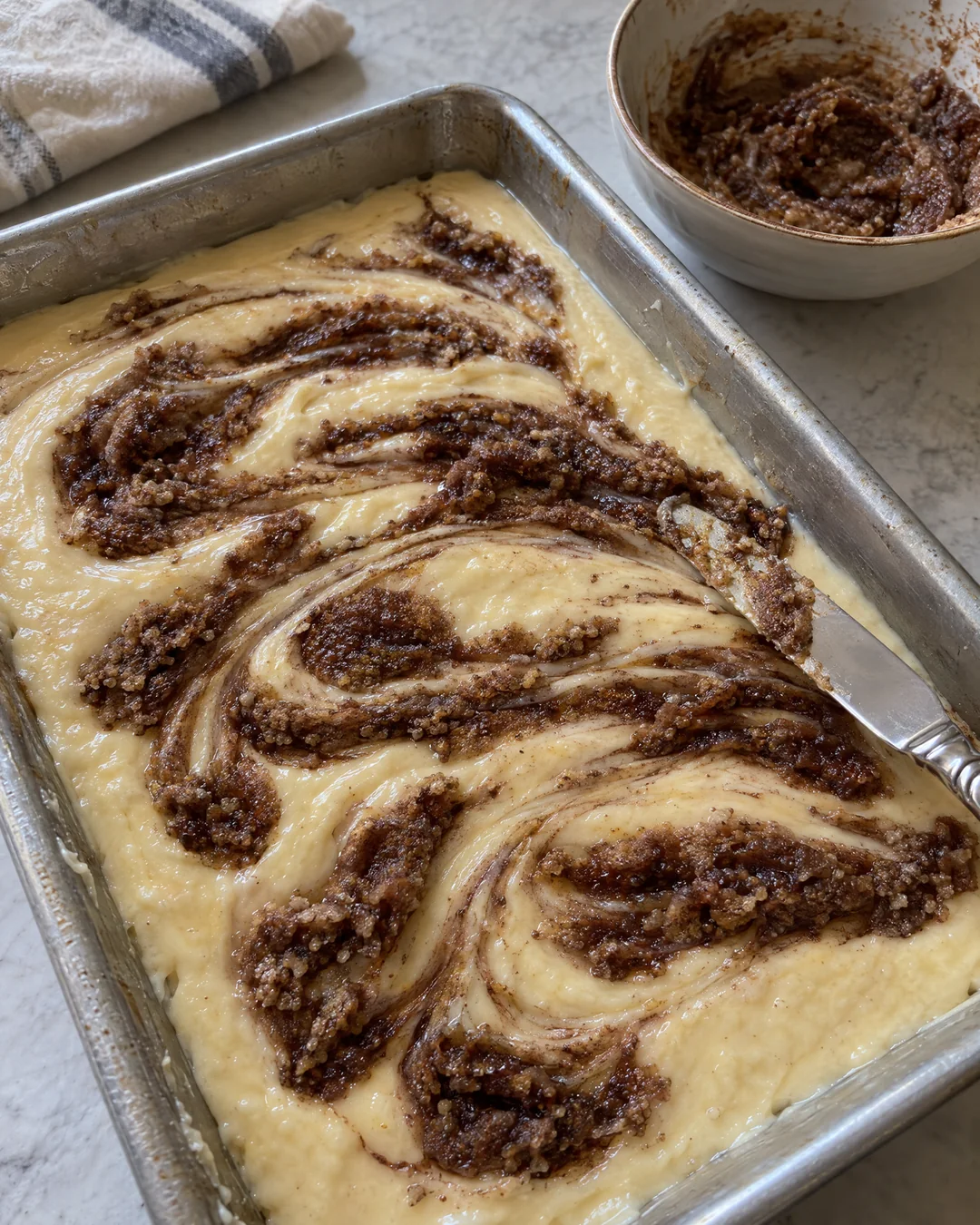 Brown sugar cinnamon swirl being dragged through cake batter with a butter knife