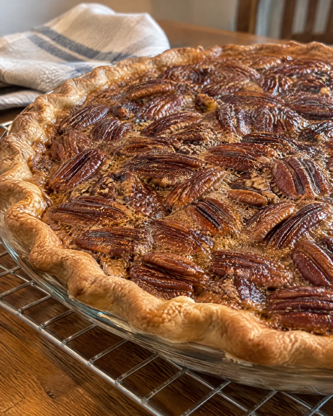 A whole baked pecan pie cooling on a rack with toasted pecans on top