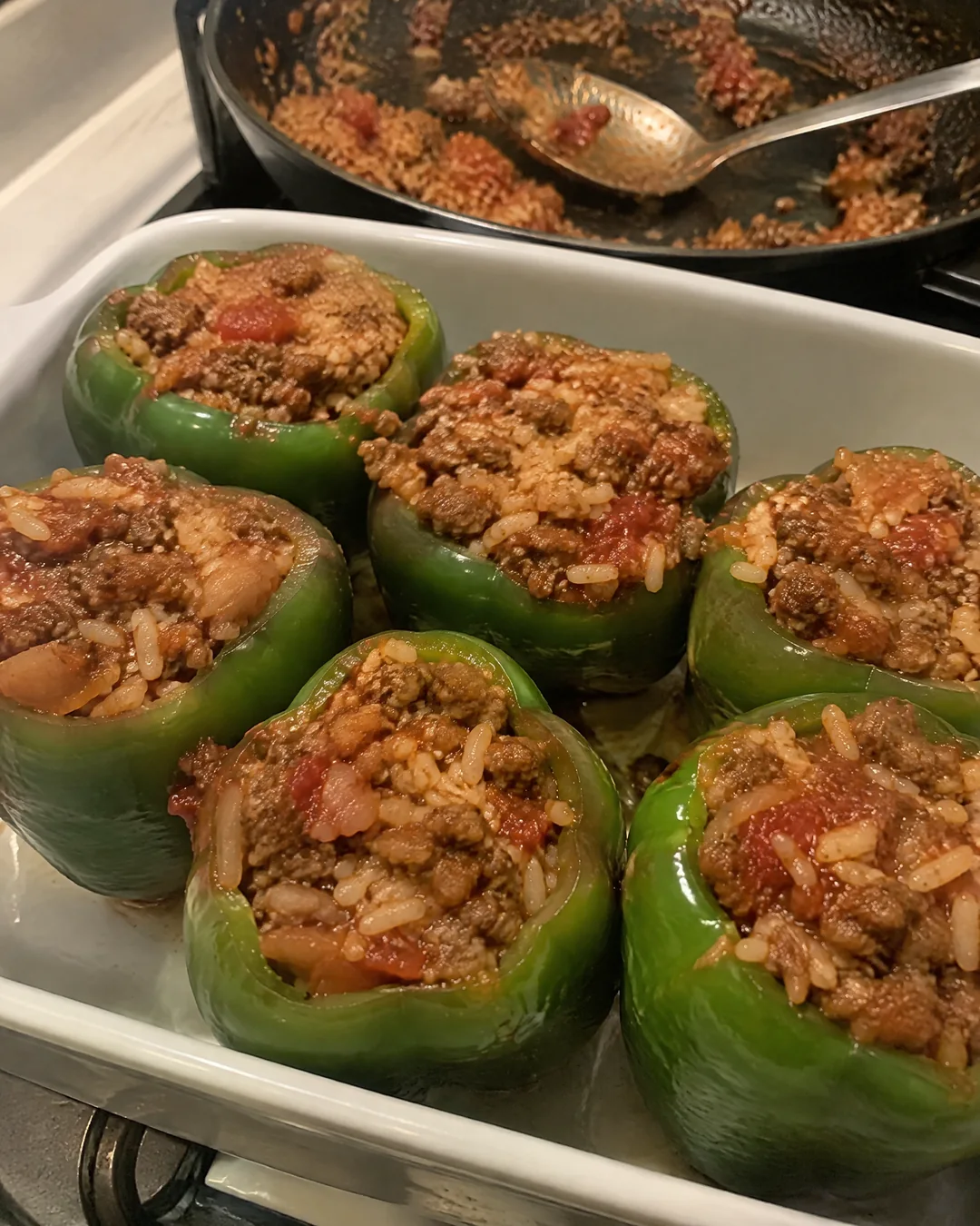 Blanched green bell peppers standing in a baking dish, filled with ground beef, rice and tomato sauce before baking