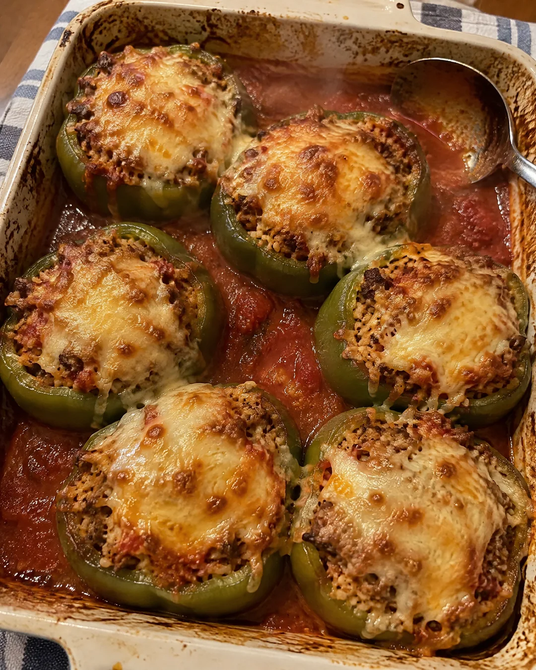 A baking dish of stuffed green peppers just out of the oven with browned melted cheese and bubbling tomato sauce, seen from above