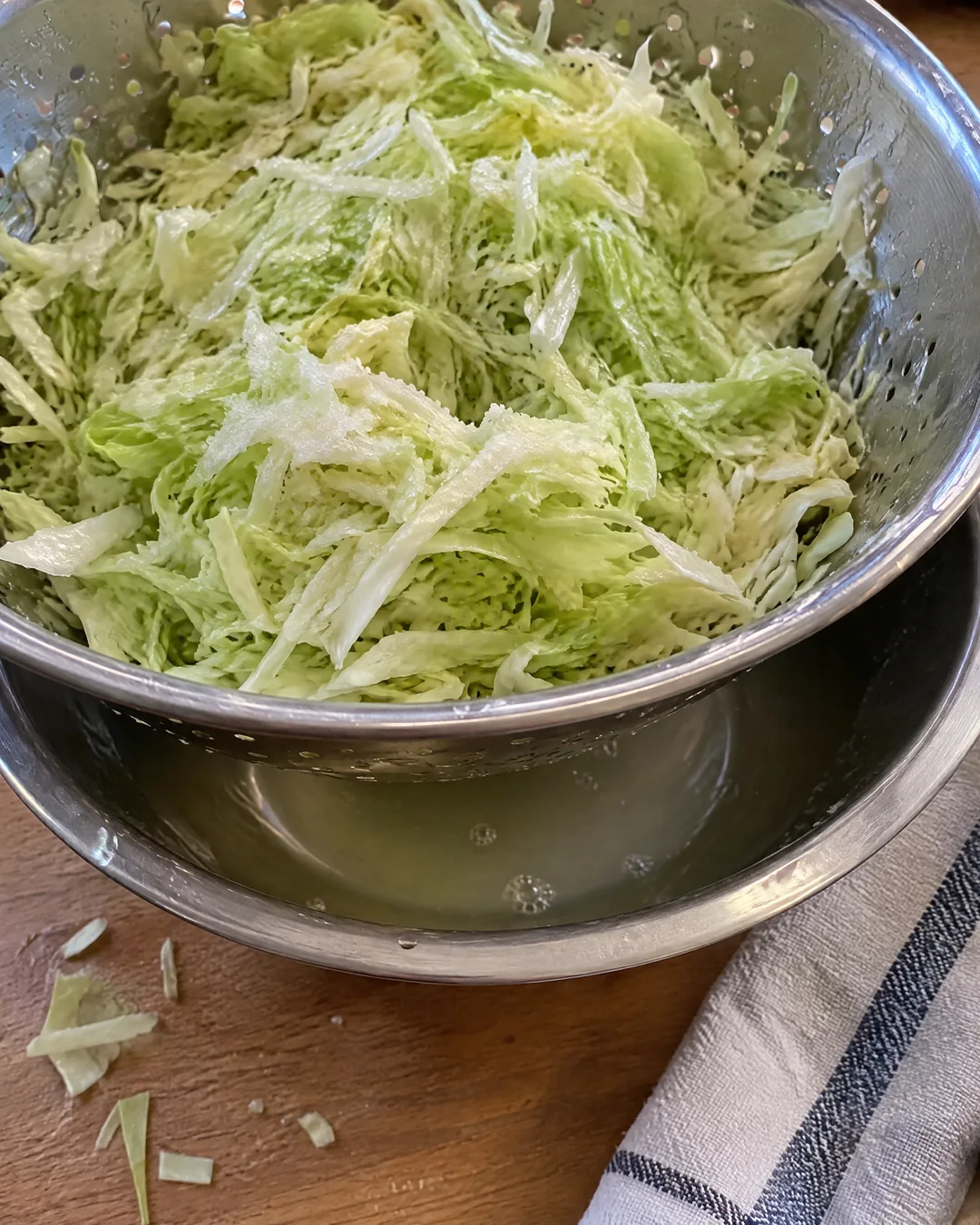Finely shredded salted cabbage draining in a colander over a bowl with water collected underneath