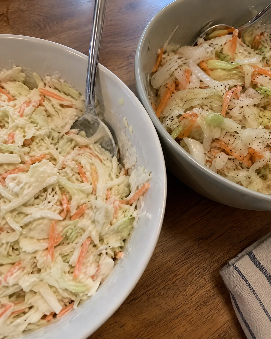 Two bowls of coleslaw side by side, one creamy white mayonnaise slaw and one glossy Carolina vinegar slaw with celery seed