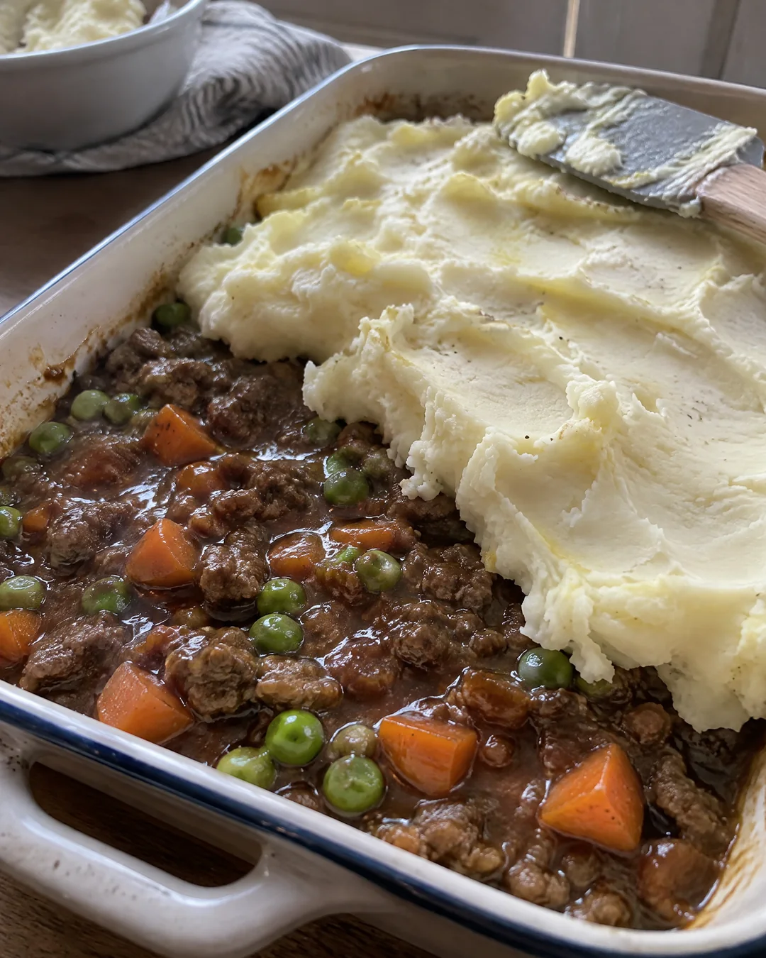 Mashed potatoes being spread over cottage pie filling