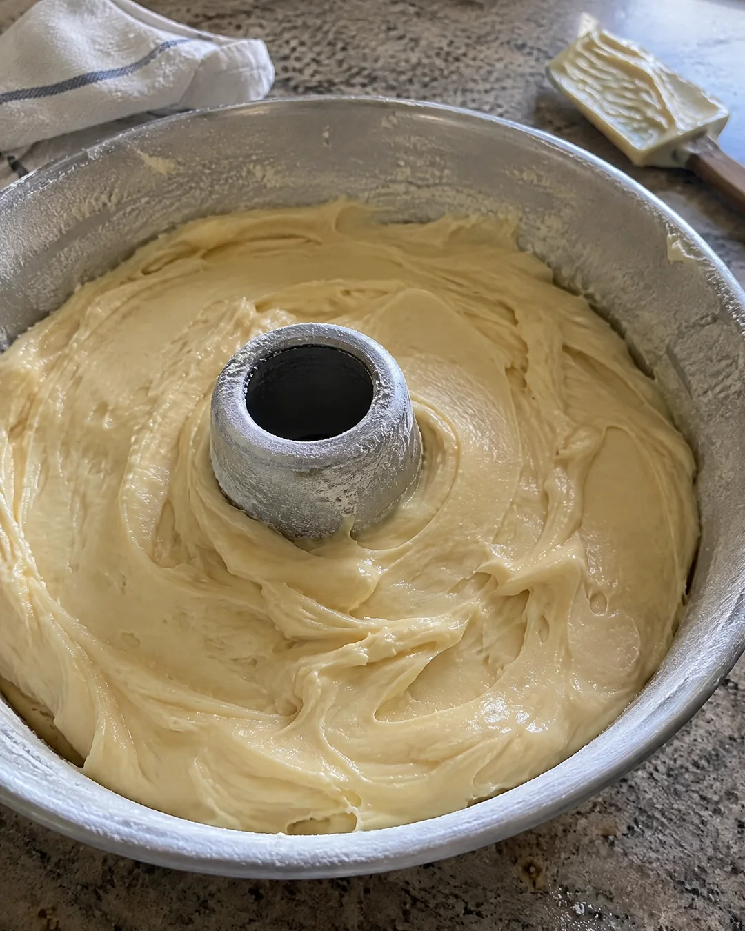 Thick cream cheese pound cake batter smoothed into a buttered and floured tube pan, ready for the cold oven