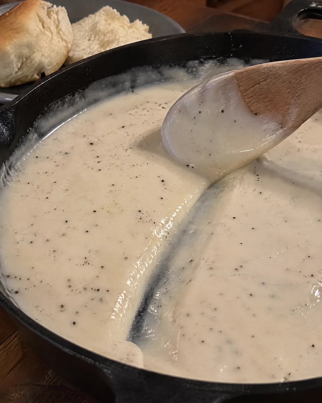 Finished smooth white cream gravy coating the back of a wooden spoon, ready for biscuits