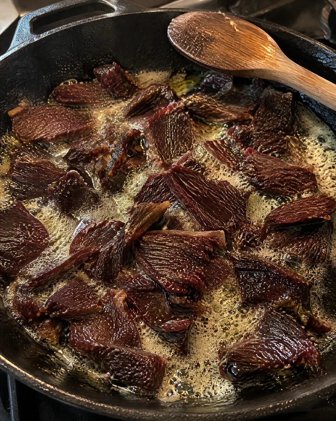 Torn ribbons of dried beef browning in foaming butter in a cast iron skillet