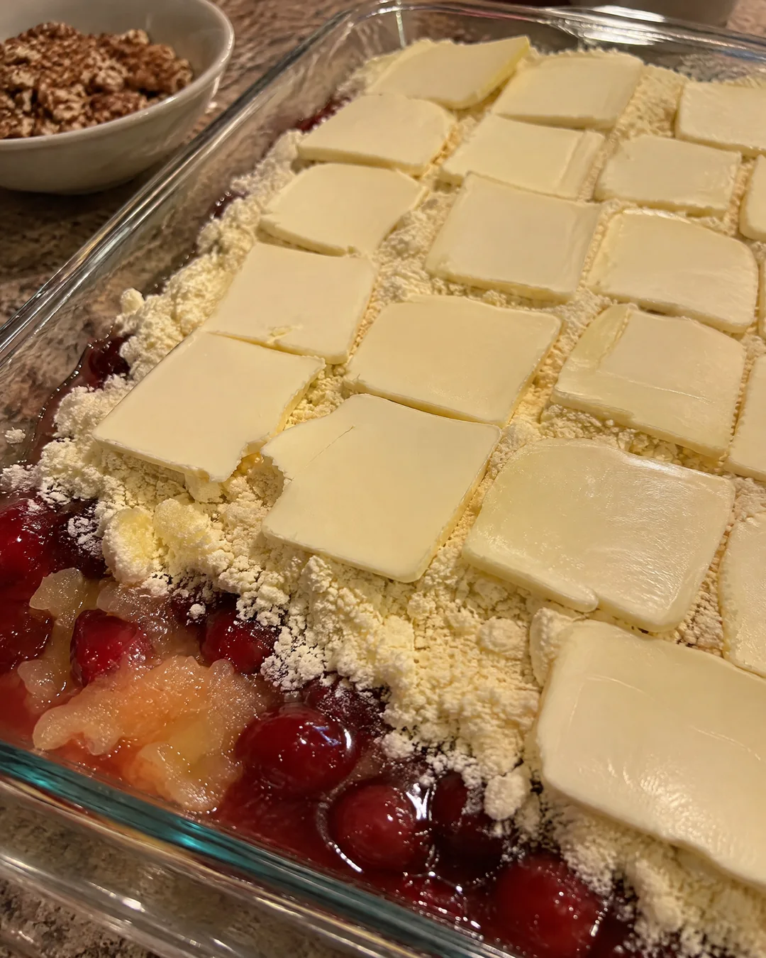 Dry yellow cake mix sprinkled over cherry and pineapple filling in a baking pan, covered with thin butter slices