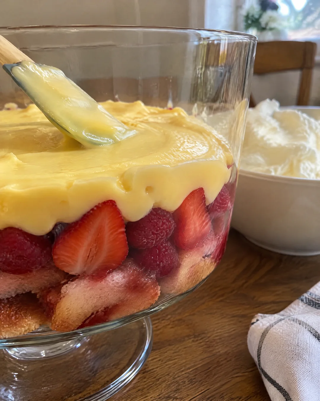 Layers of sponge, jam, berries and custard in a glass trifle bowl