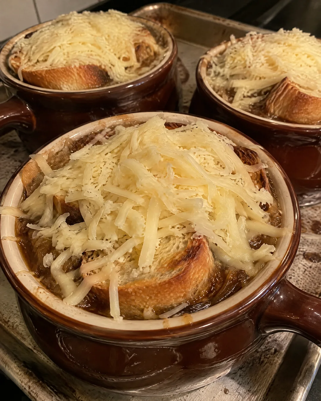 Toast and cheese being piled on crocks of onion soup