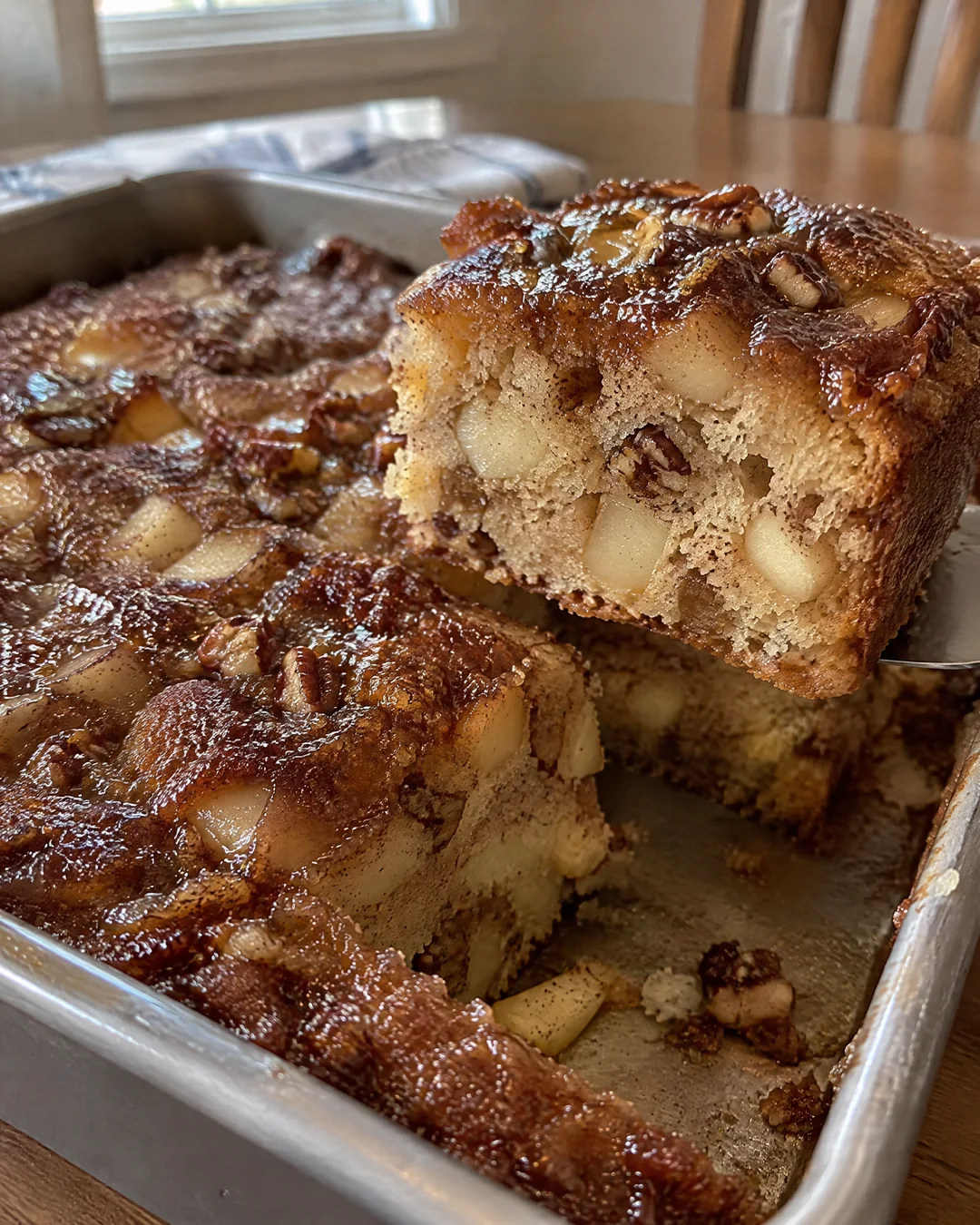 Fresh apple cake in its pan with brown sugar glaze soaked into the top, one square cut out