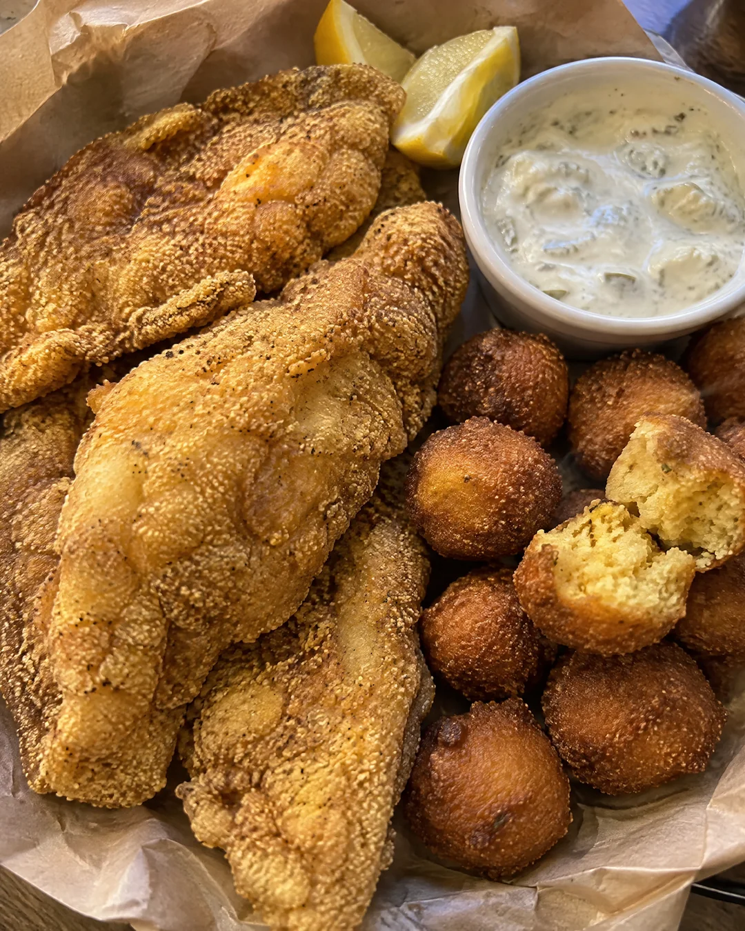A platter of fried catfish and hushpuppies on brown paper with lemon wedges, seen from above