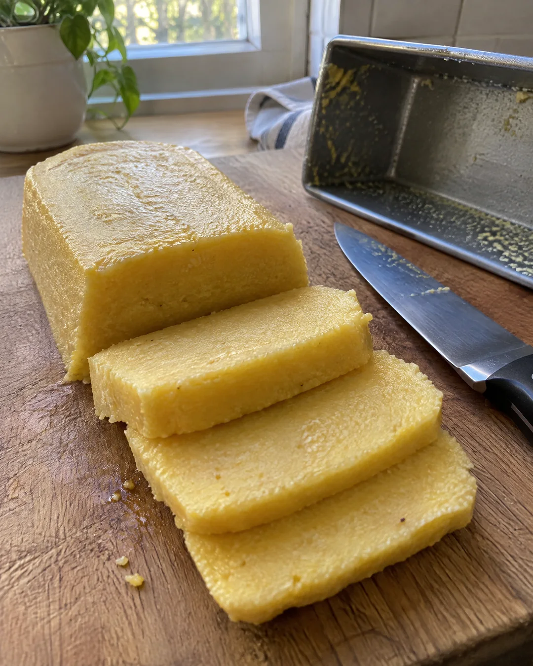 A firm block of cold cornmeal mush turned out of a loaf pan and cut into thick slices on a wooden board