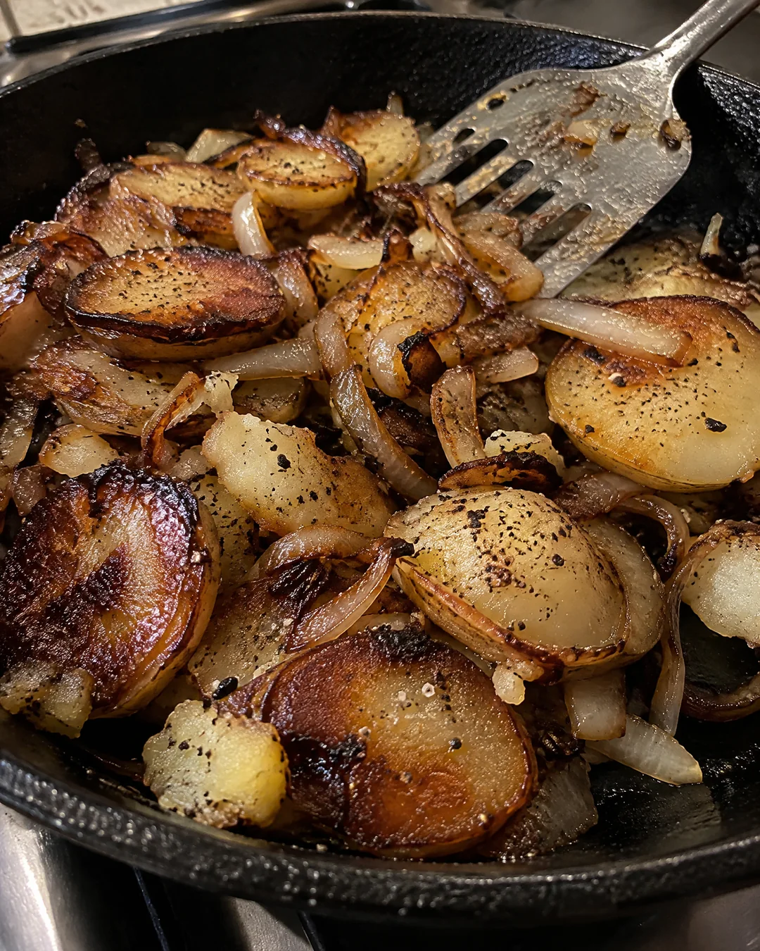 Finished fried potatoes and onions in the skillet, crisp brown potato slices and golden onions with dark edges