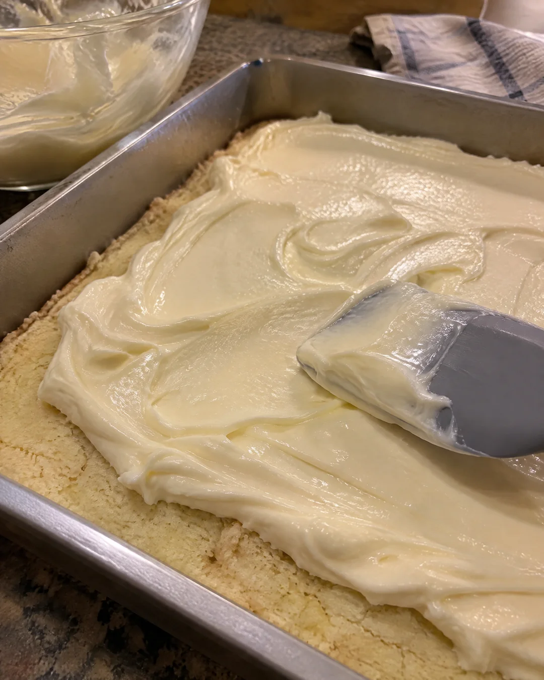Smooth cream cheese gooey layer being spread over the thin cake base in the pan