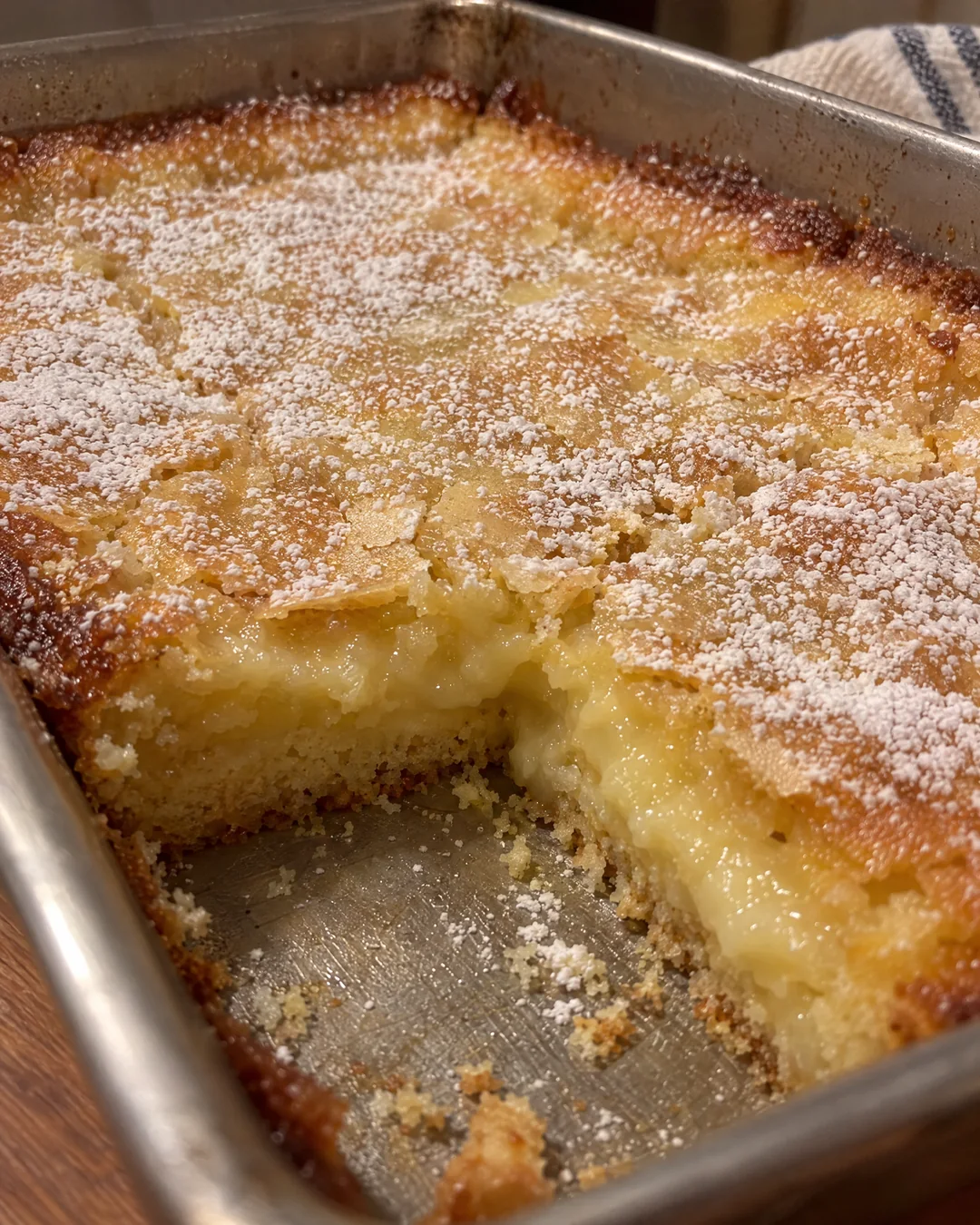 Gooey butter cake cooling in its pan, golden crackled top dusted with powdered sugar
