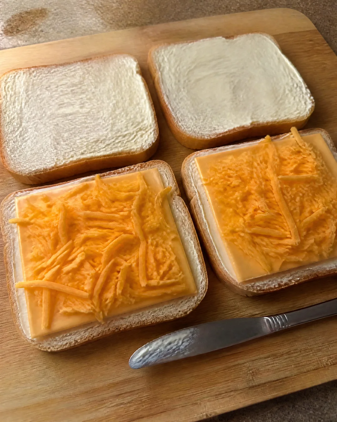 Slices of white bread spread thin with mayonnaise to the edges, cheese piled on two of them