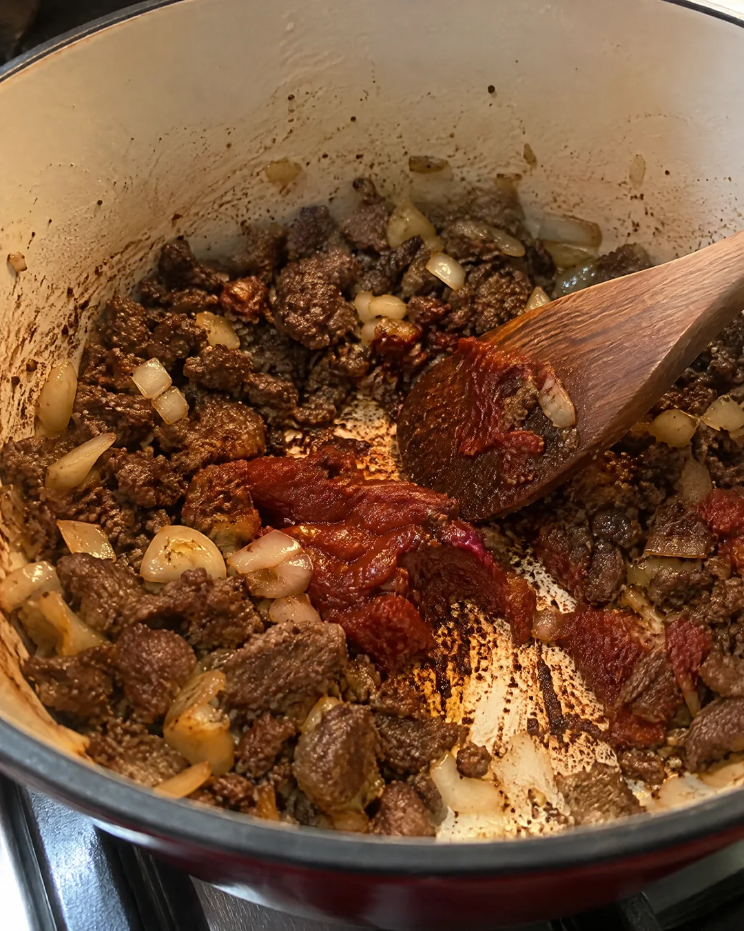 Ground beef browned dark with onion and tomato paste in a soup pot