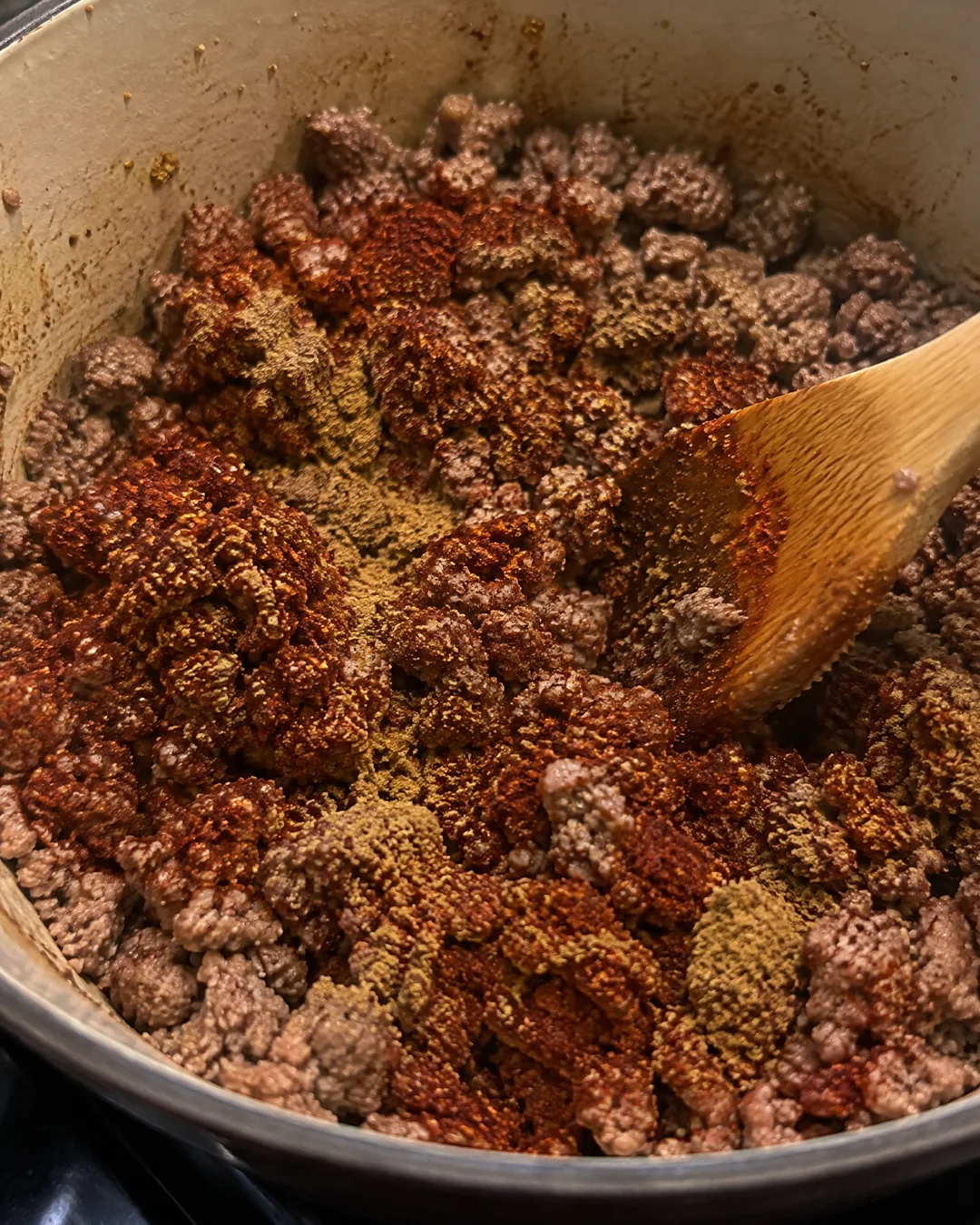 Ground beef with chili powder and cumin being stirred into the meat before the liquid goes in