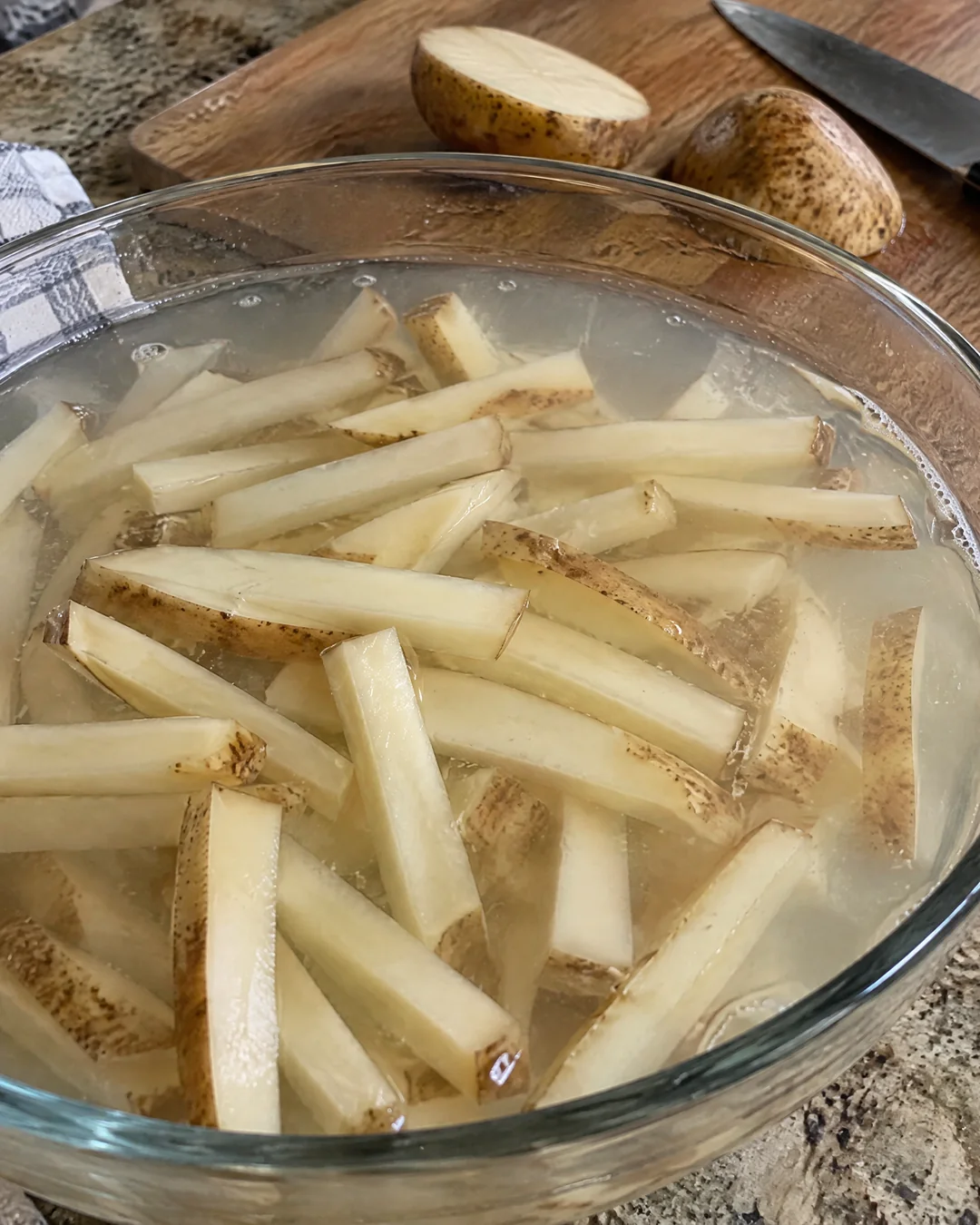 Hand-cut potato sticks soaking in a bowl of cold water